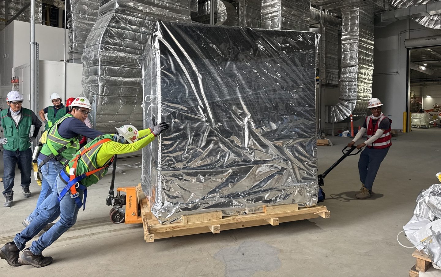 Crew moving crated equipment in on a pallet jack